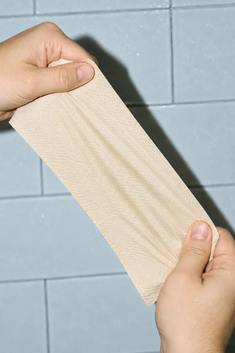 Hands holding a sheet of unbleached tan paper, showing its fine embossed texture